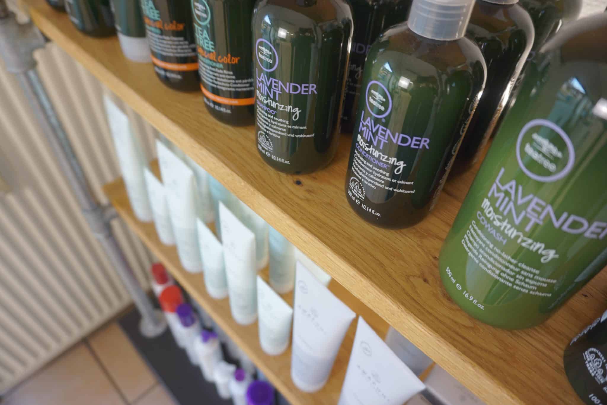 Mehrere dunkle Pflegeprodukte stehen dicht nebeneinander auf einem Holzregal.