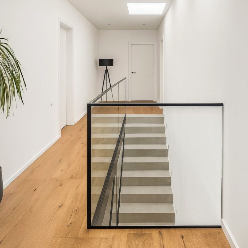 Treppengeländer aus Floatglas mit schwarzem Rahmen in modernem Flur.
