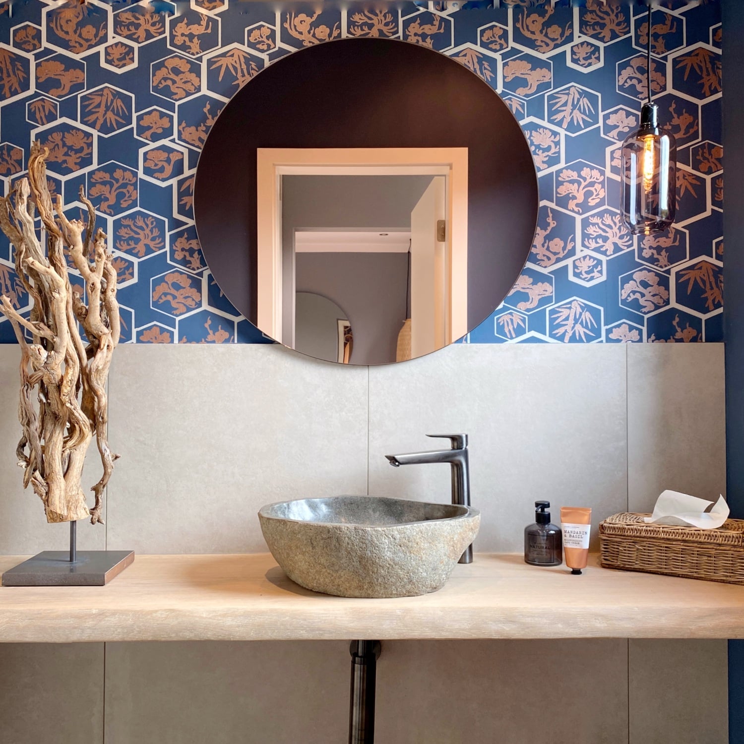Modern badkamer met houten wastafel, stenen wasbak, ronde spiegelwand en blauw behang.