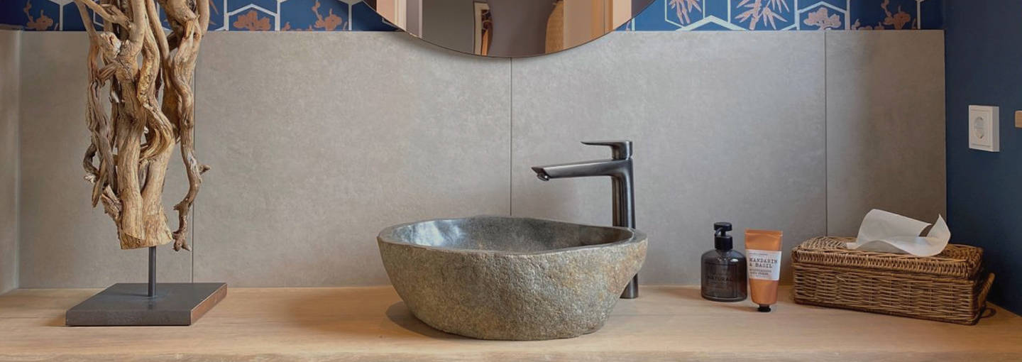 Modern badkamer met houten wastafel, stenen wasbak, ronde spiegelwand en blauw behang.