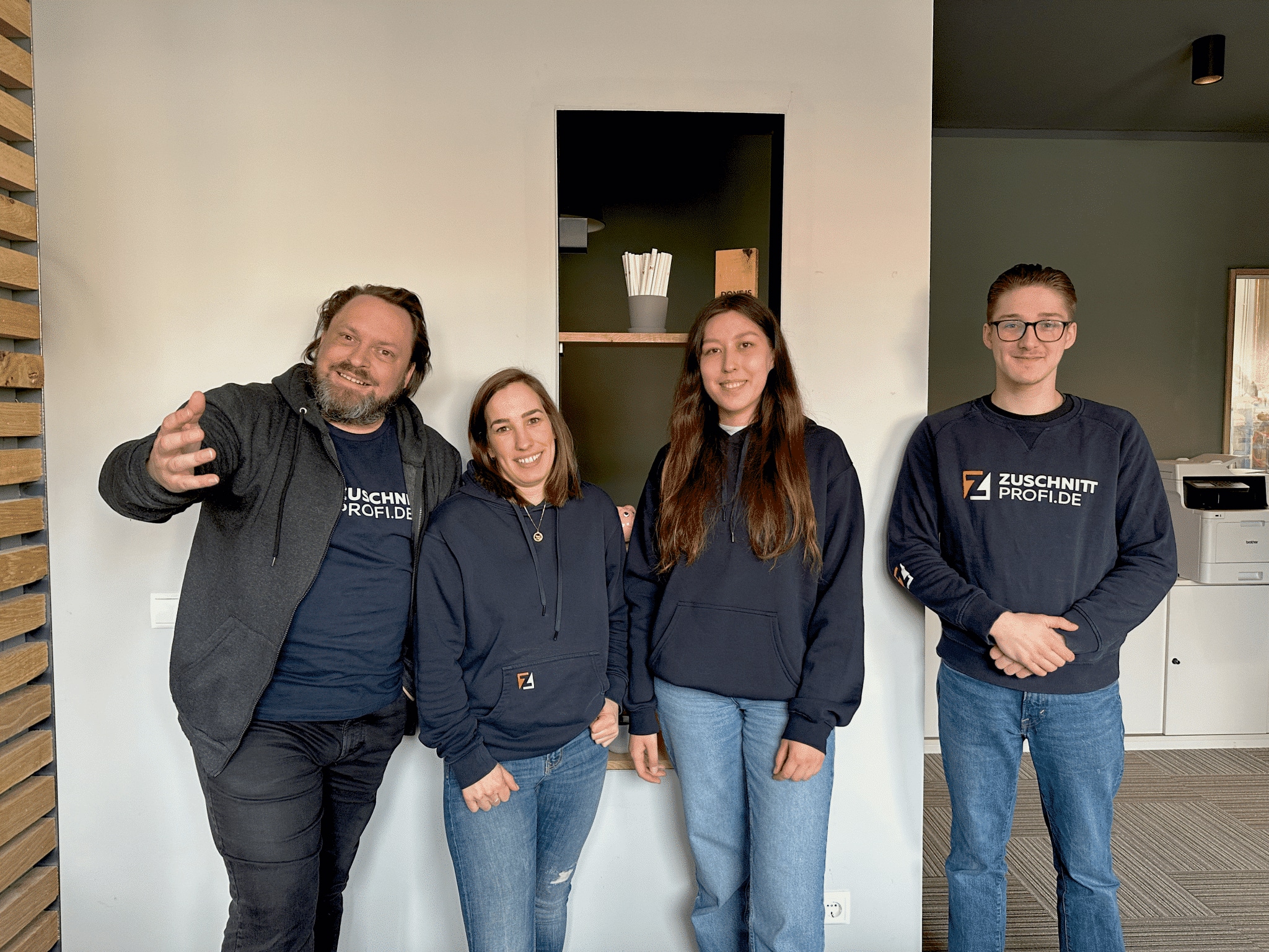 Ein Team von vier Personen von Zuschnittprofi.de steht freundlich im Bürobereich zusammen.