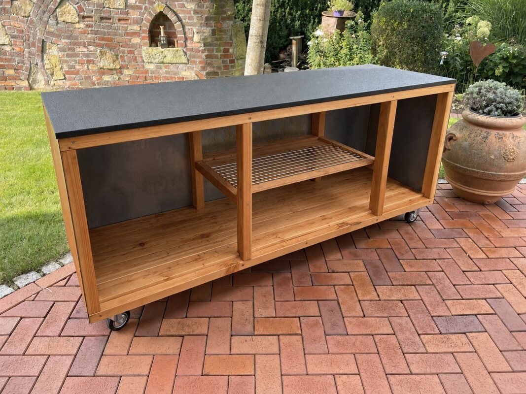 Leere mobile Outdoorküche aus Holz mit dunkler Arbeitsplatte und offenen Ablagefächern im Garten