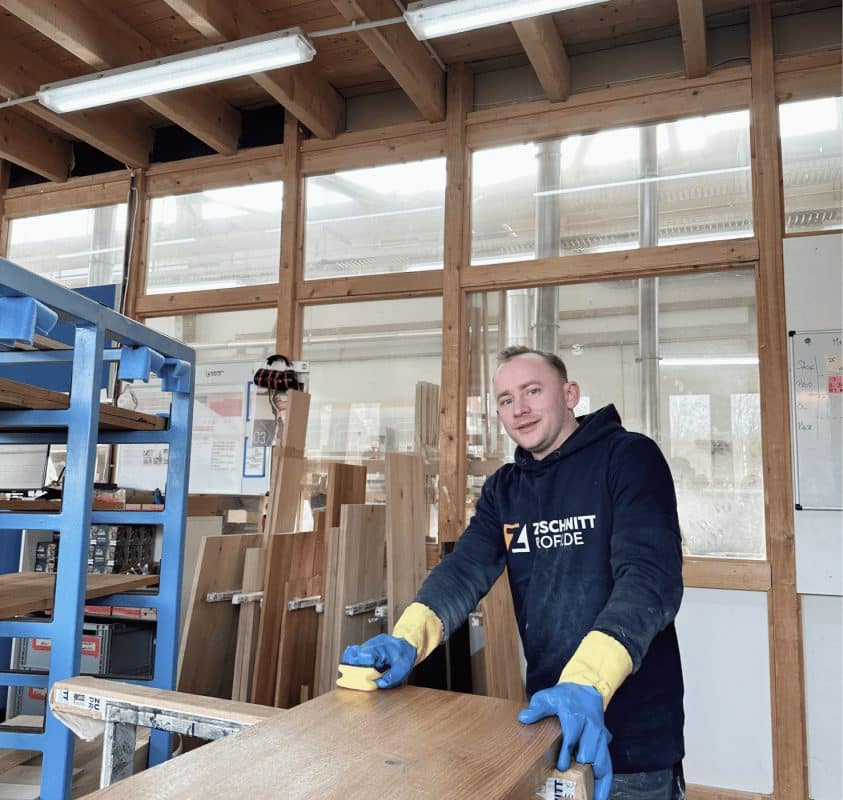Ein Mitarbeiter von Zuschnittprofi.de richtet eine massive Holzplatte sorgfältig in der Werkstatt aus.