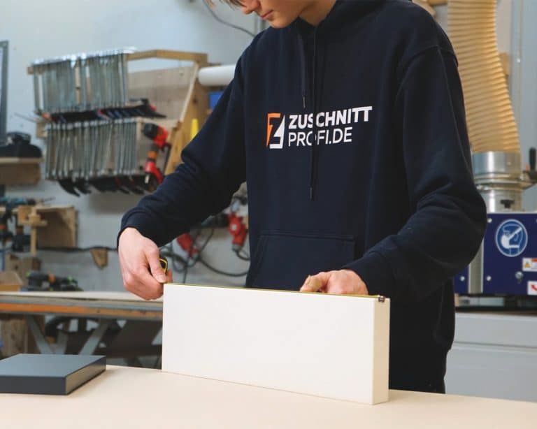 Handwerker von Zuschnittprofi.de misst weiße Platte in der Werkstatt.