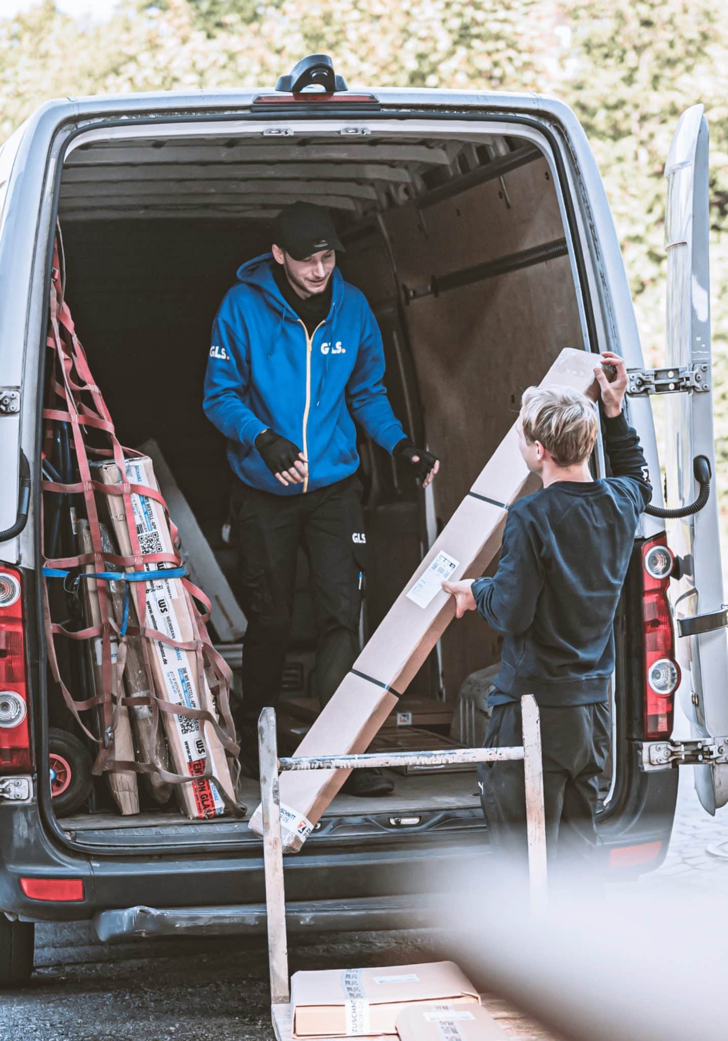 Zwei Mitarbeiter von Zuschnittprofi.de laden Material in einen geöffneten Transporter.